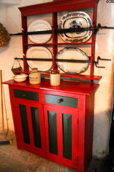 Brightly painted red & black cupboard with serving platters in Shannon Farmhouse at Bunratty Castle & Folk Park. County Clare, Ireland.