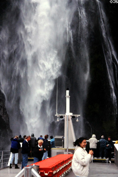 Tourist boat nosing into a waterfall in Milford Sound. New Zealand.