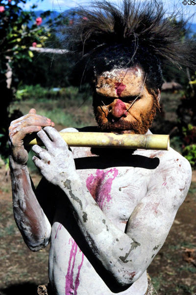 Man playing a flute-like instrument in the Mudmen village. Papua New Guinea.