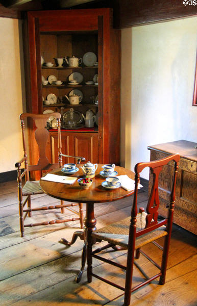 Round tea table with chairs before corner china cabinet at Stanley-Whitman House. Farmington, CT.