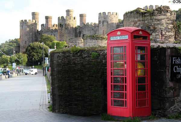 View from harbor area of castle walls & turrets with vintage red phone booth in the foreground. Conwy, Wales.