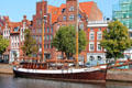 Sailing ship docked on Trave River before heritage buildings. Lübeck, Germany.