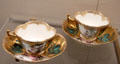 Meissen porcelain quatrefoil-shaped tea cups with gold background painted with flowers & Watteau scenes at Meissen porcelain museum at Lustheim Palace. Munich, Germany.
