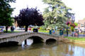 Arched footbridge crossing River Windrush in town center. Bourton-on-the-Water, England.