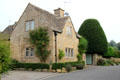 Cotswold stone home with slate roof & climbing red roses on side. Lower Slaughter, England.