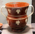 Red earthenware loving cup with applied molded relief decoration made in Straffordshire at Potteries Museum & Art Gallery. Hanley, Stoke-on-Trent, England.