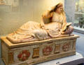 Etruscan carved terracotta cinerary urn with reclining woman with open lidded mirror on lid & columns & flowers on chest from near Chiusi at British Museum. London, United Kingdom.