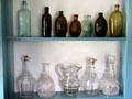 Early American glass bottles, pitcher & decanters in Noon Inn Barroom at Old Bethpage Village. Old Bethpage, NY.
